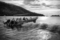 Black-and-white photograph of people boarding a canopy-covered boat in shallow coastal water, with breaking waves and wooded hills in Costa Rica.