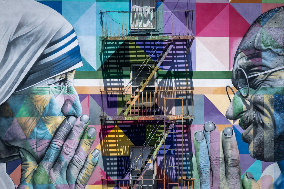 Colorful mural of two facing figures with hands held together, separated by a metal fire escape and its shadows in New York.