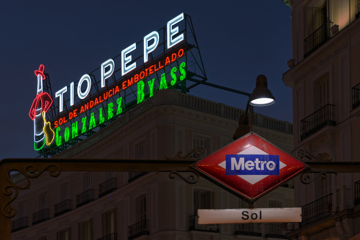 Illuminated Tio Pepe neon sign above the red-and-blue Sol Metro entrance sign in Madrid at night.
